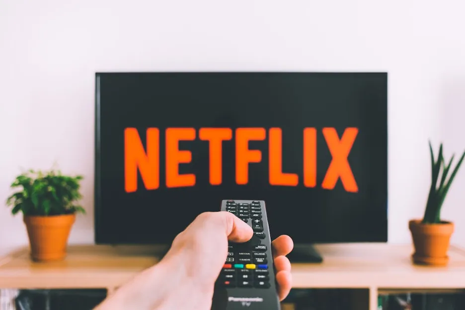 A hand holding a remote control in front of a television Description automatically generated