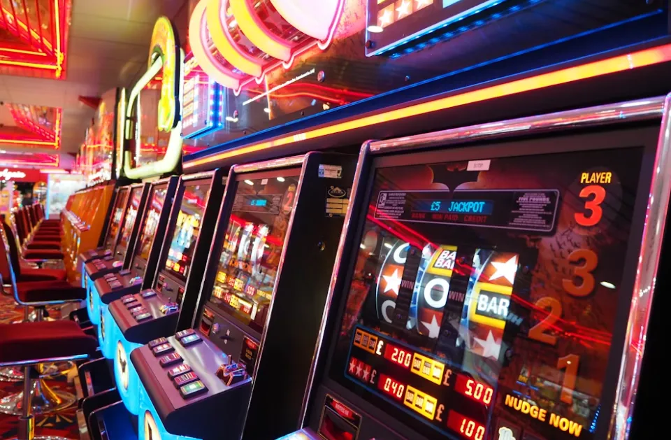Row of illuminated casino slot machines with colorful screens in a gaming arcade